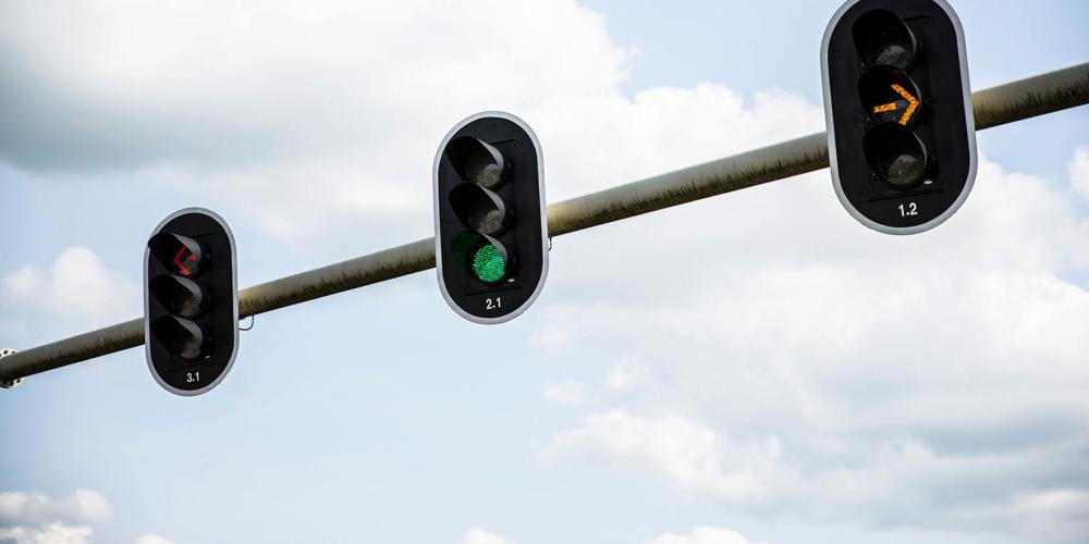 Drie verkeerslichten aan een paal met rood (naar links), groen (rechtdoor) en oranje licht (rechtsaf)