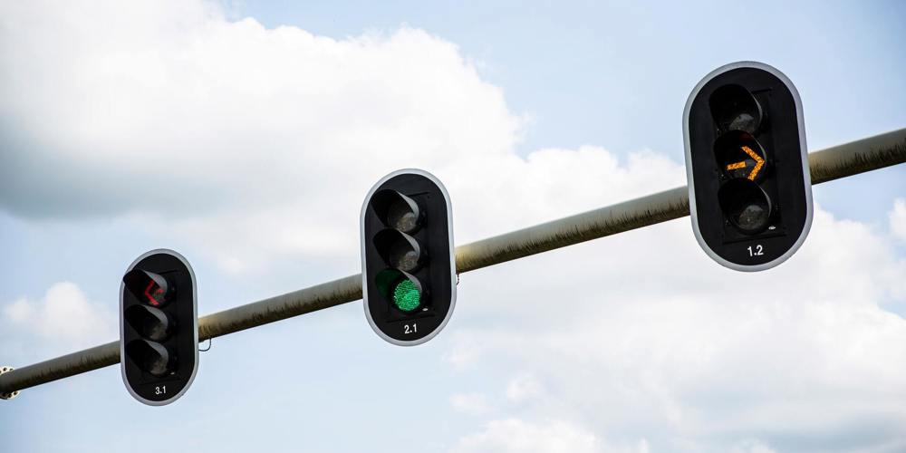 Drie verkeerslichten aan een paal met rood (naar links), groen (rechtdoor) en oranje licht (rechtsaf)