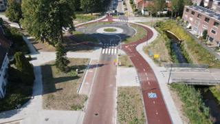 Luchtfoto van een rotonde in de heringerichte Bankastraat in Hengelo, met doorgetrokken fietspaden en woonwijk op de achtergrond.