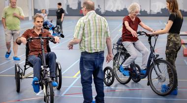 Groep mensen in gymzaal met fietsen en driewielers. Foto DigiDaan - Fietsersbond