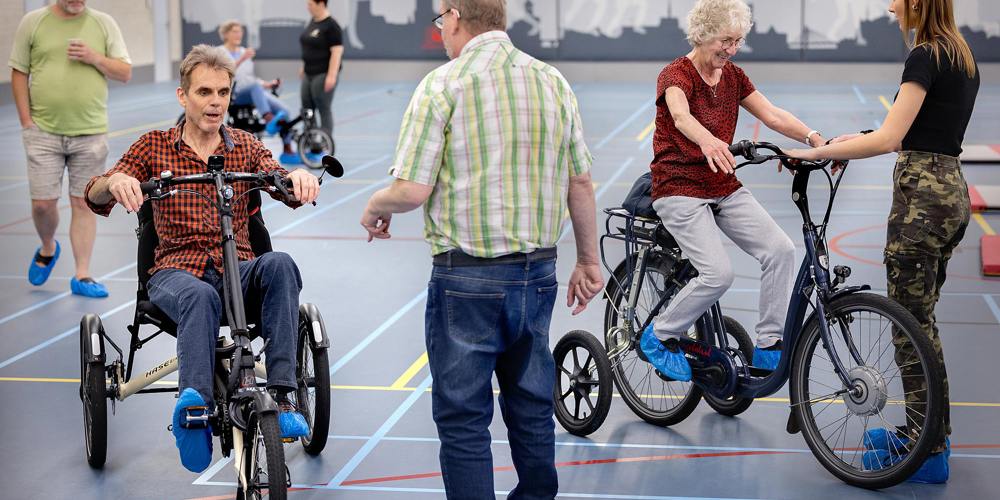 Groep mensen in gymzaal met fietsen en driewielers. Foto DigiDaan - Fietsersbond