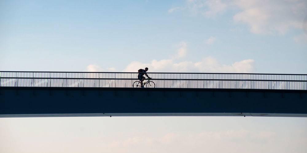 Fietser op een brug met hekwerk, onder een deels bewolkte lucht.