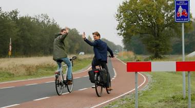 Twee fietsers op fietspad zwaaien.