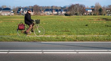 Man fietst over een fietspad met huizen en een veld op de achtergrond - Foto Serhat Beyazkaya - Unsplash