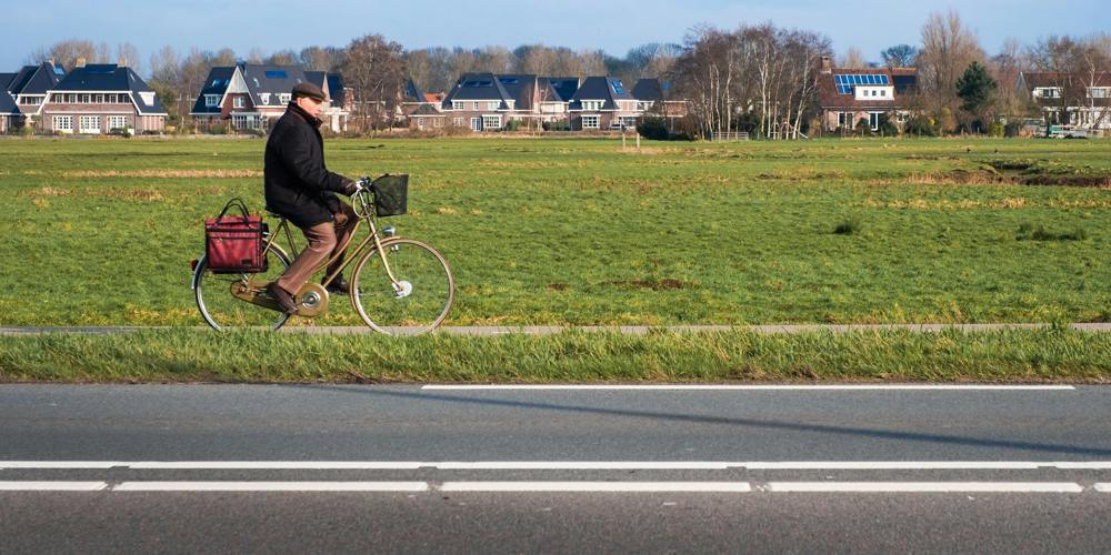 Man fietst over een fietspad met huizen en een veld op de achtergrond - Foto Serhat Beyazkaya - Unsplash