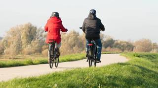 Twee mensen fietsen op een pad door een groen landschap.