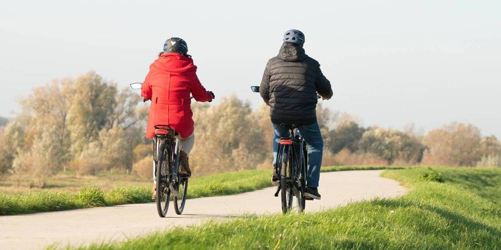 Twee mensen fietsen op een pad door een groen landschap.