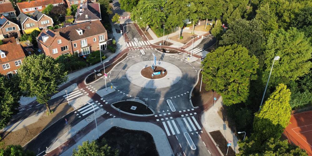 Luchtfoto van een rotonde met fietspaden, zebrapaden en omliggende huizen en bomen.