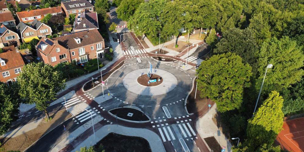 Luchtfoto van een rotonde met fietspaden, zebrapaden en omliggende huizen en bomen.