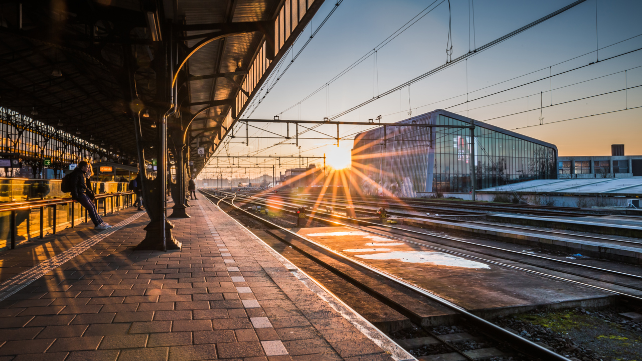 Treinstation bij zonsopgang met zonnestralen over de sporen.