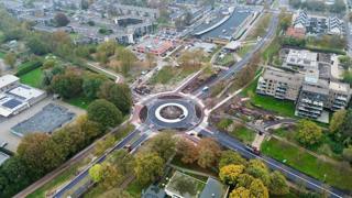Luchtfoto van een rotonde in een stedelijk gebied met wegen, gebouwen en groen.
