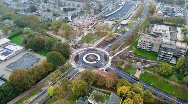 Luchtfoto van een rotonde in een stedelijk gebied met wegen, gebouwen en groen.