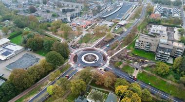 Luchtfoto van een rotonde in een stedelijk gebied met wegen, gebouwen en groen.