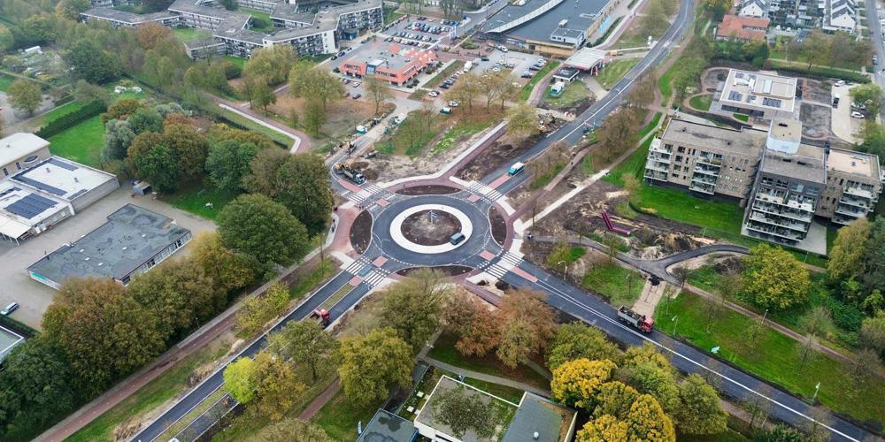 Luchtfoto van een rotonde in een stedelijk gebied met wegen, gebouwen en groen.