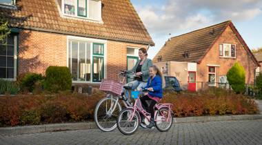 Een vrouw en een jong meisje fietsen samen door een woonwijk.
