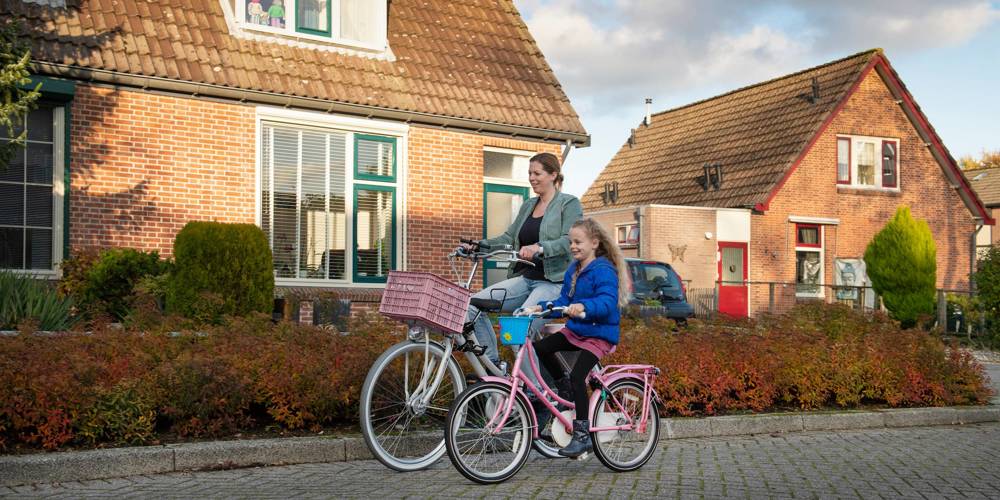 Een vrouw en een jong meisje fietsen samen door een woonwijk.