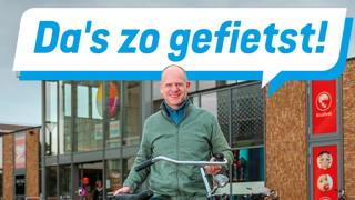 Man met fiets voor winkelcentrum, met tekstballon: Da's zo gefietst!