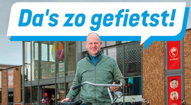Man met fiets voor winkelcentrum, met tekstballon: Da's zo gefietst!