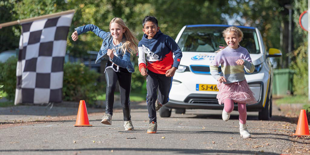 Drie kinderen rennen lachend over de weg richting een finishlijn.