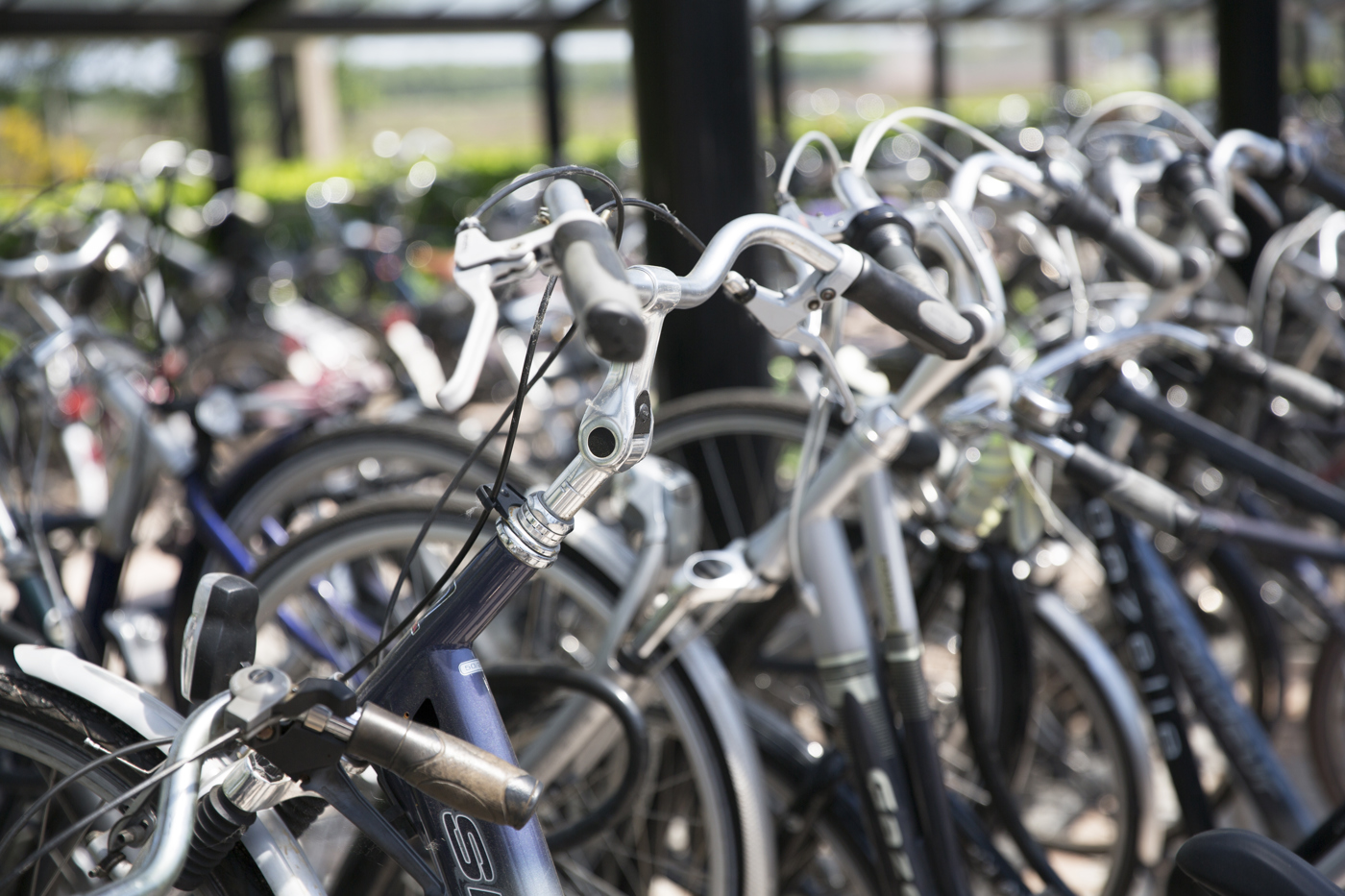 Fietsenstalling met vooraan in beeld een close-up van een rij fietssturen. Op de achtergrond staan onscherp nog meer fietsen gestald.
