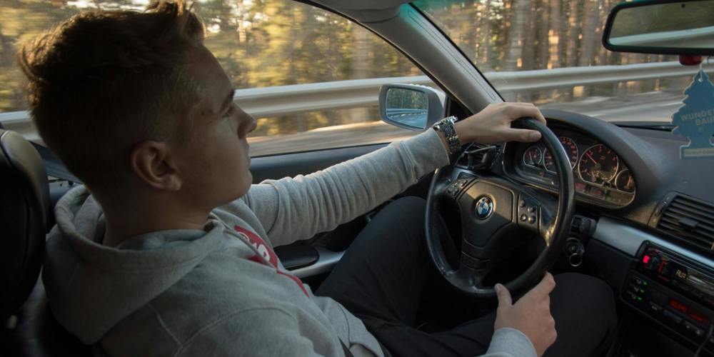 Jongeman in grijze hoodie rijdt in BMW. Fotograaf Sol Jansson - Unsplash