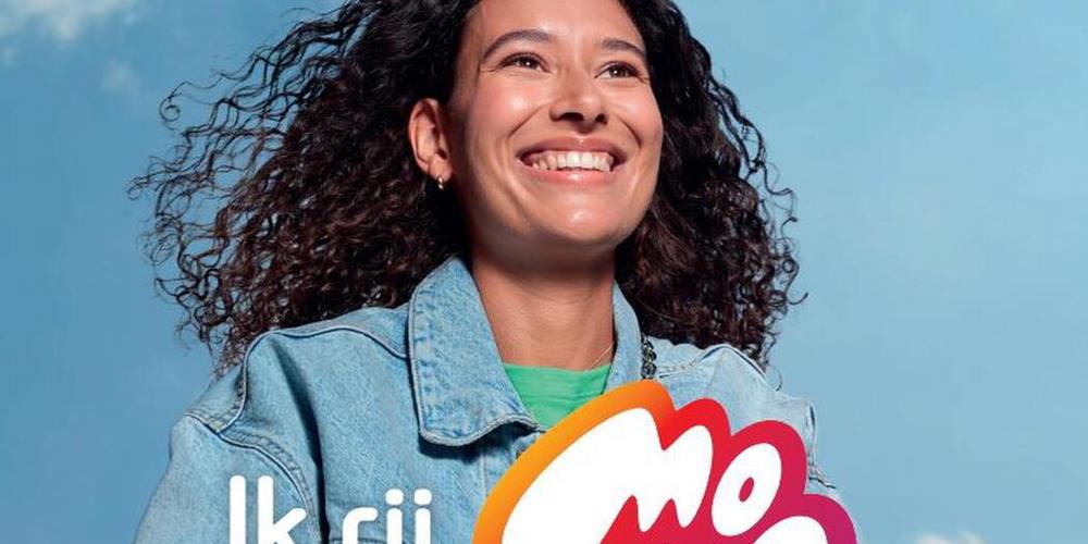 Een lachende vrouw fietst buiten, met een helderblauwe lucht op de achtergrond. De tekst "Ik rij MONO" is links en rechts van de vrouw geplaatst en de woorden "Kom veilig thuis" zijn aan de onderkant van de afbeelding te zien.