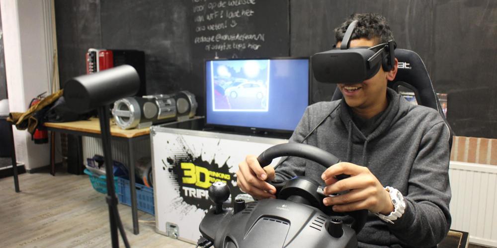 Persoon met VR-headset en stuurcontroller simuleert autorijden in kamer met monitor, speakers en apparatuur.