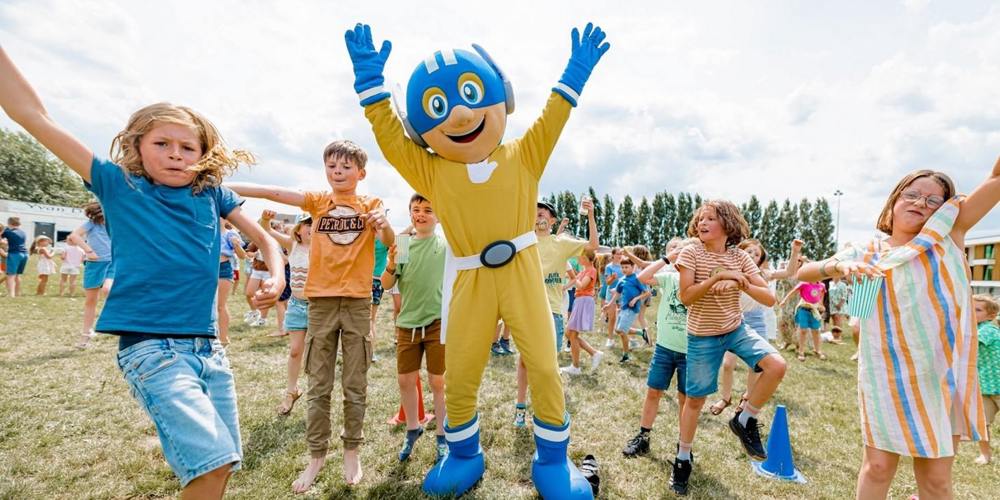 Kinderen springen blij in de lucht op een grasveld samen met een vrolijke mascotte in geel-blauw pak.