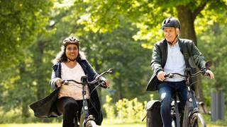 Twee mensen van middelbare leeftijd fietsen samen in een groene omgeving.