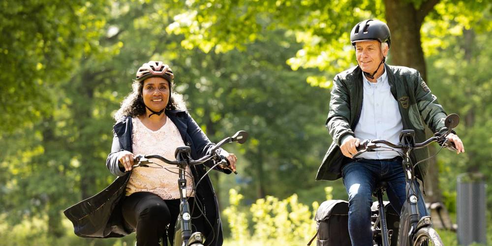 Twee mensen van middelbare leeftijd fietsen samen in een groene omgeving.