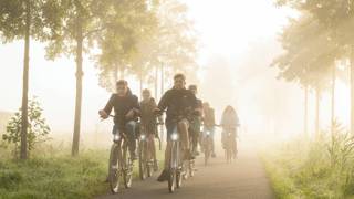 Een groep jongeren fietst samen over een mistige weg, omringd door bomen.