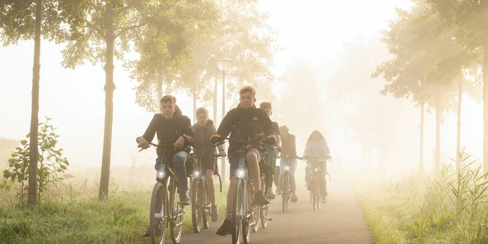 Een groep jongeren fietst samen over een mistige weg, omringd door bomen.