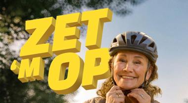 Een vrouw zet haar fietshelm op met de tekst 'ZET 'M OP' in beeld.