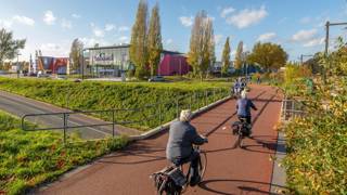 Fietsers op een rood fietspad langs een bioscoop op een zonnige dag.