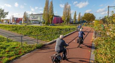 Fietsers op een rood fietspad langs een bioscoop op een zonnige dag.