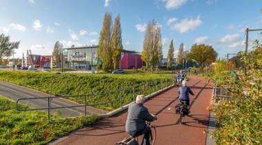 Fietsers op een rood fietspad langs een bioscoop op een zonnige dag.