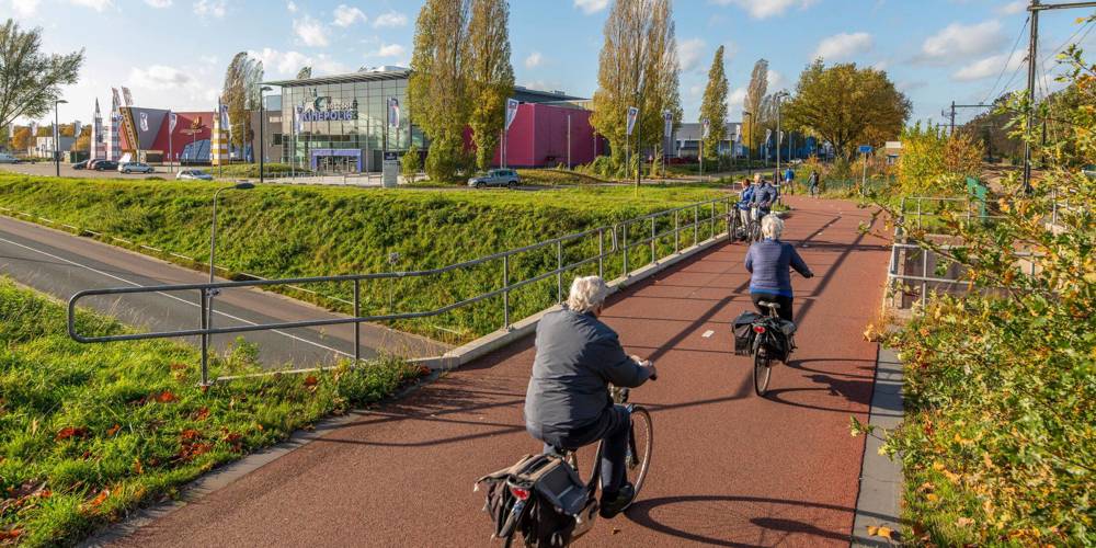 Fietsers op een rood fietspad langs een bioscoop op een zonnige dag.
