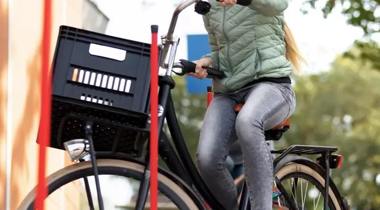 Een meisje op een fiets met een krat voorop, fietst tussen rode paaltjes door.