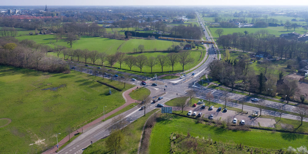 Drukke kruising in landelijk gebied met auto's en omliggende velden.