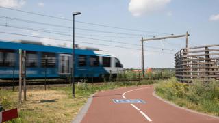 Blauwe trein rijdt langs een fietspad onder een blauwe lucht.