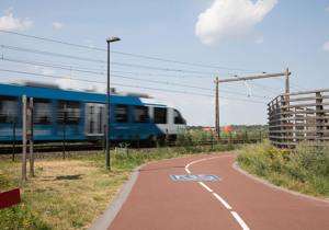 Blauwe trein rijdt langs een fietspad onder een blauwe lucht.
