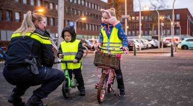 Agent praat met twee kinderen op fiets en loopfiets met veiligheidshesjes.