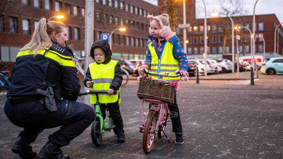 Agent praat met twee kinderen op fiets en loopfiets met veiligheidshesjes.
