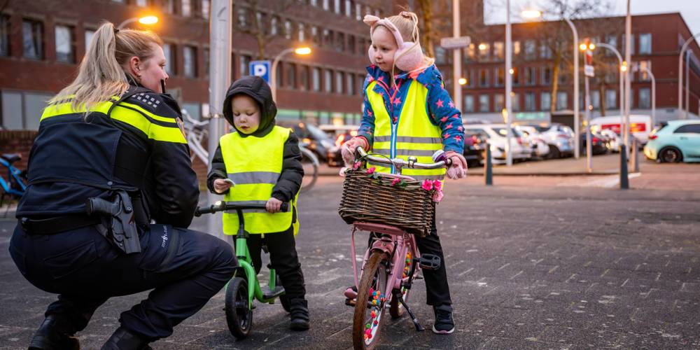Agent praat met twee kinderen op fiets en loopfiets met veiligheidshesjes.