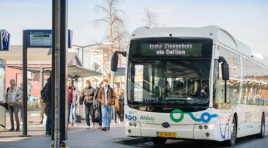 Elektrische bus van RRReis bij een drukke bushalte, met reizigers die instappen of wachten.