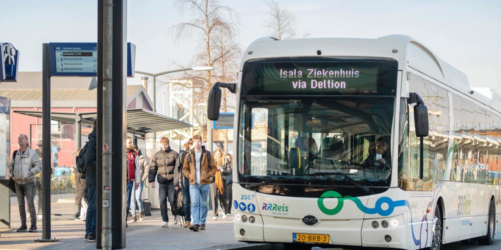Elektrische bus van RRReis bij een drukke bushalte, met reizigers die instappen of wachten.